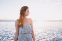 young woman standing on a beach looking to her side 