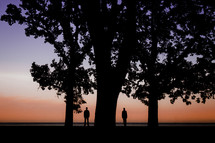Two people standing beside a large tree at sunset