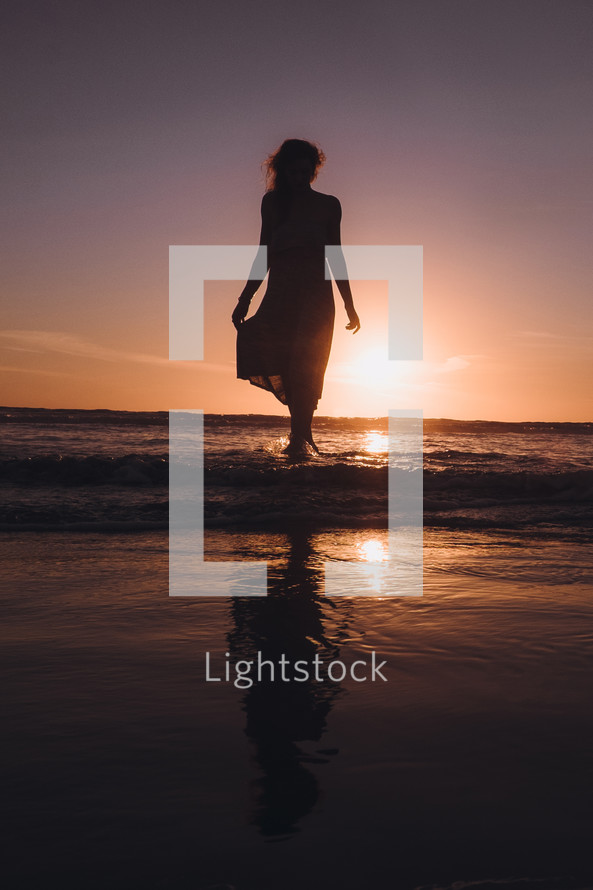 young woman walking into the ocean at sunset 