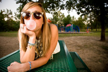 teen lying on top of a table blowing a bubble
