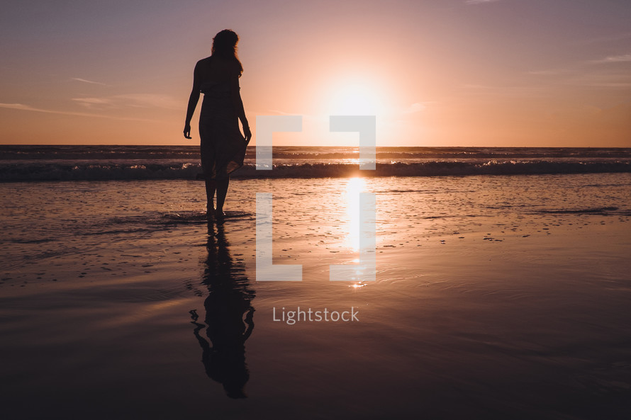young woman standing on wet sand on a beach at sunset 