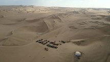 Aerial shot drone flies high over dune buggy parking lot and sand dunes stretching out in the distance near desert city oasis Huacachina, Peru