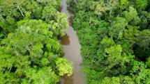 Aerial shot drone lowering with camera panning up as canoe full of people paddling down brown river in middle of Amazon rainforest approach the camera