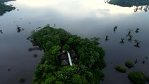 Aerial shot drone pans left around indigenous village on peninsula jutting out into black lagoon in middle of Amazon rainforest just before sunset