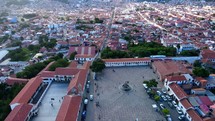 Aerial shot drone flies backwards over mirador plaza at top of hill overlooking city revealing large white church