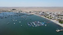 Aerial shot drone flies over inflatable aquatic park toward the desert in Paracas National Reserve