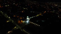 Aerial shot drone flies in semicircle to left around well lit church in a night time Quito