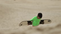 Boy struggling to climb up sand dunes hill with sand board after going down - success