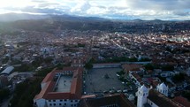 Aerial shot drone flies forward over large white church and mirador plaza at top of hill overlooking city