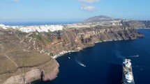 Aerial shot drone orbits to the right around cruise ship docked in Santorini as tender boat drives to ship