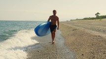 Boy walks with sup board in the waves of the sea