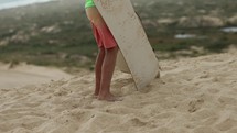Boy struggles to walk sand boards across sand dunes as rain begins - outdoor activities