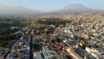 Aerial shot drone flies to right over Arequipa with Misti Volcano and Chachani Volcano at dusk in the distance