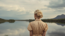 AI Generated Image. Rear back view on a blond woman wearing vintage dress and looking to the pond