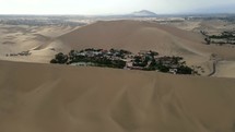 Aerial shot drone slowly descends behind sand dune in front of desert city oasis Huacachina, Peru