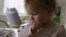 Toddler girl sitting on table pointing taste testing different donuts - close up on face