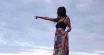Young cool hippy looking woman pointing off into distance with cloudy skies behind her