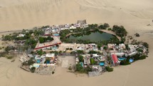 Aerial shot drone orbits to the left around entire desert city oasis of Huacachina, Peru