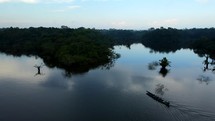 Aerial shot drone slowly lowering over water as canoe boat on black lagoon in middle of Amazon rainforest just before sunset passes through