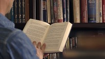 a man picking a book from a bookshelf and reading 