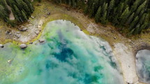 drone flying over beautiful reflective glacier lake surrounded by trees in Dolomites in Italy