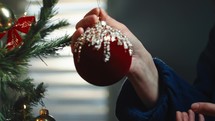 Girl is hanging a red Christmas ball on the tree in the house