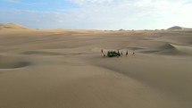 Aerial shot drone flies backwards over endless sand before passing over a dune buggy in desert city oasis Huacachina, Peru
