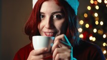 Girl drinks a cup of hot chocolate against the Christmas tree