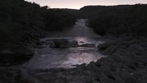 Drone flies over pool at waterfall at Ribeirão do Meio in Chapada Diamantina just after sunset with pink sky