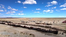 Aerial shot drone flies up and away from train cemetery in middle of desert on sunny day with blue sky
