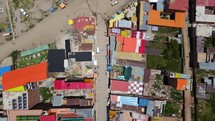 Aerial shot drone flies to left with camera facing down over brightly colored roofs of buildings next to boat marina