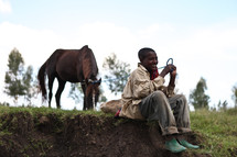 Ethiopian boy sitting and letting a horse graze 