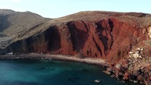 Aerial shot drone flies away from Red Beach with two sail boats in bay in the south of Santorini