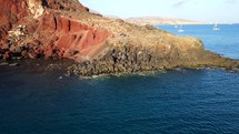 Aerial shot drone flies up and away from clear blue waters at Red Beach in the south of Santorini