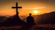 Silhouette of a person praying on his knees on a mountain with crucifix at sunrise in morning 