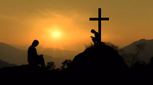 Silhouette of a person praying on his knees on a mountain with crucifix at sunset 