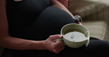 Pregnant woman sits on couch drinking tea
