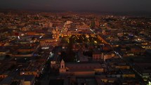 Aerial shot drone flies over Plaza de Armas in Arequipa with sunset behind camera