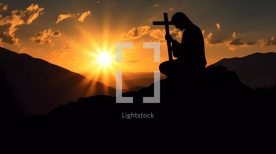 Silhouette of a person praying on his knees on a mountain with crucifix at sunset 