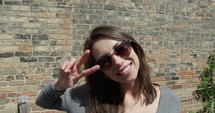 Millennial woman shows peace sign with hands against brick background - extreme close up 