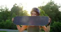 Female skateboarder holding skateboard in hands at skatepark during sunset