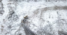 Skipper tractor in field dragging trees in deforested area on winter day - aerial shot
