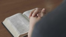Man reading a Bible with hands clasped in prayer.