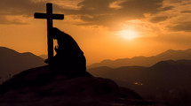 Silhouette of a person praying on his knees on a mountain with crucifix at sunrise 