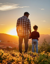 Father and child hold hands while watching a golden sunset in the evening for Fathers Day.