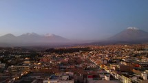 Aerial shot drone flies over Arequipa at sunset toward Misti Volcano and Chachani Volcano