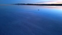 Aerial shot drone wide shot orbits left toward facing the sunset on reflective water
