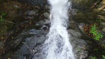 Aerial shot drone flies with camera straight down over the top of a waterfall in a forest.
