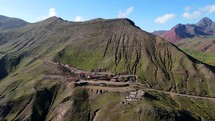 Aerial shot drone orbits up and to right in wide shot of parking lot for hikers to ascend Rainbow Mountain with Red Valley in the background