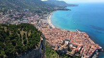 Aerial shot drone flies from behind La Rocca down to the city of Cefalu, Sicily, Italy